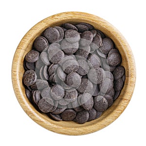 Dark unsweetened chocolate chips in wooden bowl isolated on white. Top view