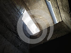 Dark ventilation shaft with sunlight through a metal grid shows concrete exchanger airway for basement and big facilities