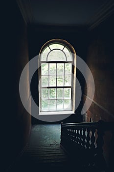 Dark vintage staircase interior in old building, stair with wooden railing, big window with day light