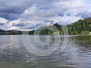 dark water of lake near Church of the Holy Trinity in Slovenske Gorice under cloudy sky. Slovenia