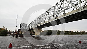 Dark wide river with bridge and construction area with concrete beems and cranes