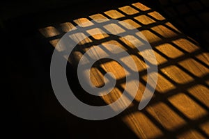 Dark window bars shadow on the wooden floor in prison