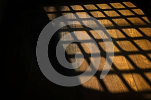 Dark window bars shadow on the wooden floor in prison