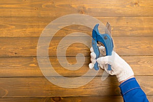 On a dark wooden background, a workerâ€™s hand in white gloves, holds blue scissors for cutting materials, there is a place for