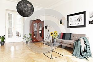 A dark, wooden, display cabinet by a white wall of an eclectic living room interior with yellow sunflowers and art