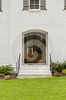 Dark wooden front door with a small arch and black rails with green grass