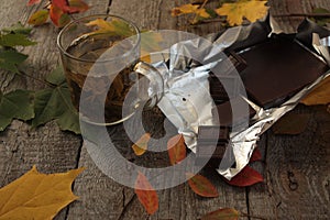 On the dark wooden table hot green tea, chocolate, apples, plums, raspberry, book. autumn or winter evening.