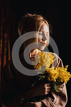 In the darkness, a middle-aged woman sits tormenting, her smile like a beacon, holding a bouquet of yellow flowers