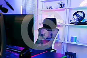 Darkroom for a professional gamer with a comfortable empty gamer chair, computer table, neon lights, keyboard, monitor,