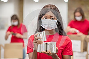 Darkskinned girl in protective mask with canned food