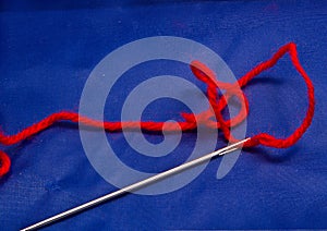 Darning needle, red wool, blue background.