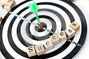 Dart arrow on center of dartboard and Success Text made of wood on the desk