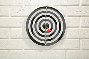 Dart Board on the white wall background. Red dart arrow hitting in the center of dartboard