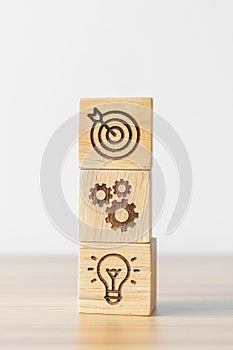 Dartboard above Gear and Lightbulb icon block on desk. business planning process, goal, strategy, target, mission, action,