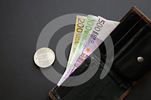 Dash coin next to Euro bank notes sticking out of a wallet on black background. Digital currency, block chain market. Euro bills