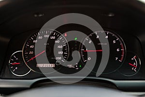 The dashboard of the car is glowing blue with red arrows at night with a speedometer, tachometer and other tools to monitor the