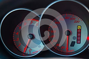 The dashboard of the car is glowing blue with red arrows at night with a speedometer, tachometer and other tools to monitor the