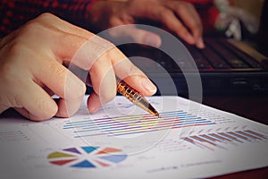 Data analyzing with laptop and pointing pen at charts and graph