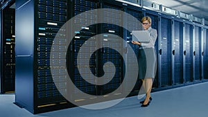 In Data Center: Female IT Technician Stands Near Rack Cabinet and Runs Maintenance Program on Lapt