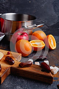 The dates on a board, oranges and apples and a metal saucepan on the table. Indoors. Side view.