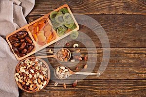 Dates, dried apricots and kiwis in a Compartmental dish and assortment of nuts in wooden bowl on a dark wooden table