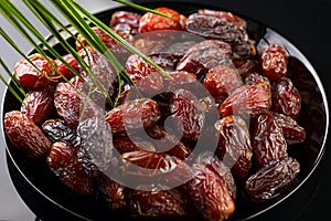 Dates fruit. Date fruits with palm tree leaf on black background. Big plate full of Medjool dates close up