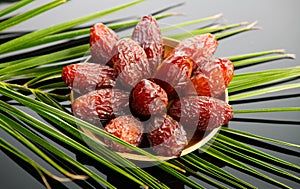 Dates fruit. Date fruits with palm tree leaf on black background. Heap of Medjool dates in wooden bowl