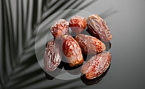 Dates fruit. Date fruits with palm tree leaf, in a wooden bowl, on black background. Medjool dates