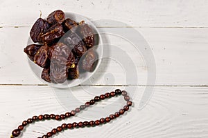 Dates fruit and rosary on white wooden table. Top view