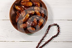 Dates fruit and rosary on white wooden table. Top view