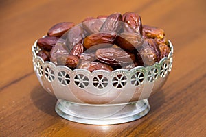 Dates fruit on a silver bowl on wooden table. The Muslim feast of holy month of Ramadan Kareem