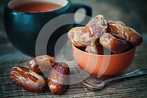 Dates fruits in bowl and tea cup on background.