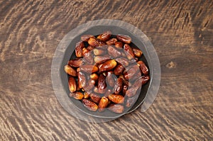 Dates in a plate on wooden background. Dried fruit on a brown table. Copy space, top view, flat lay