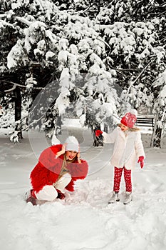 Daughter blows snow from a spruce branch onto her mother. mom and daughter blonde on a background of snow and large Christmas