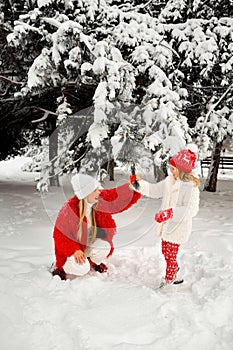 Daughter blows snow from a spruce branch onto her mother. mom and daughter blonde on a background of snow and large Christmas