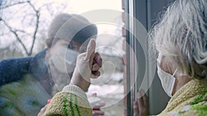 Daughter congratulates her mother on quarantine gift through glass. Mom shows off thumb for joy