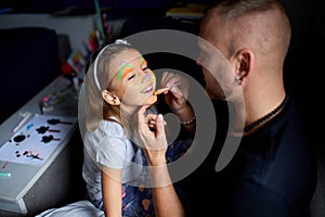 Daughter and father paint a face, having fun, leisure together at home