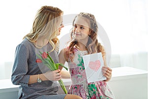 Daughter gave her mother a bouquet of tulips and a postcard made with her own hands. Happy motherhood