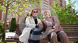 Daughter and grandmother talking and laughing sitting on a bench in autumn.