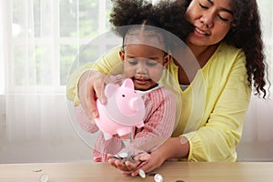 Daughter and happy mother saving money putting coin of cash into piggy bank