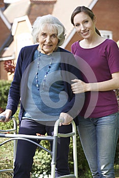 Daughter Helping Senior Mother To Use Walking Frame