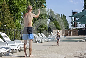 Daughter and her dad playing near the pool. Little girl in swimsuit and hat playing ball near the pool