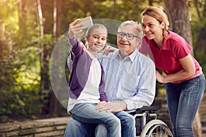 daughter with her disabled father in wheelchair and granddaughter using phone for selfie.