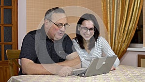 A daughter and her father communicate with friends via video communication through a laptop. A young woman and an old