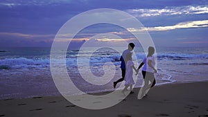 Daughter holding hands of dad and mom on the beach running on sandy shore at sunset Amazing light sunset or sunrise sky watching s