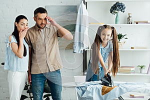 daughter holding iron above burned shirt at home