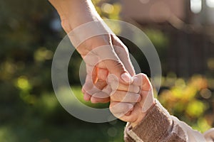 Daughter holding mother`s hand outdoors, closeup view