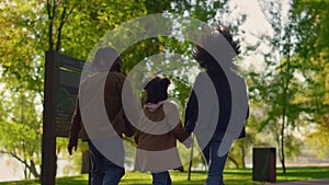 Daughter holding parents walking green park path rear view. Joyful leisure time