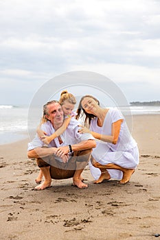 Daughter hugging father. Husband and wife hunkering down on the sand. Relation between parents and daughter. Family concept. Spend