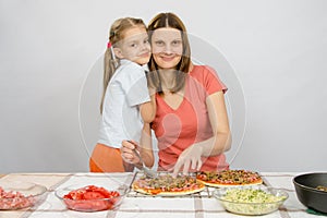 Daughter hugging her mother, which makes pizza